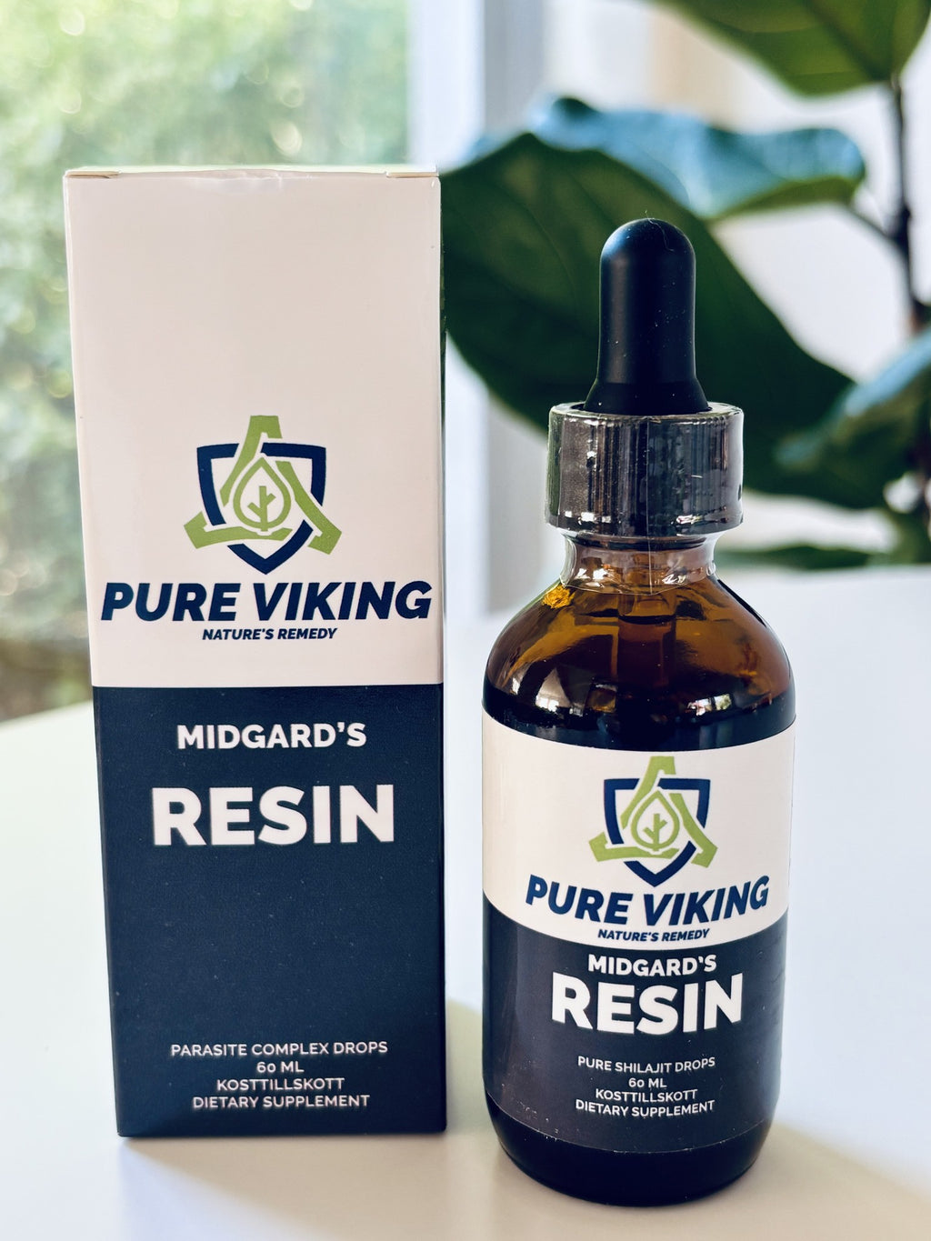 Midgard's Resin shilajitdroppar, 60 ml brun glasflaska med pipett bredvid mörkblå och vit kartong vid gröna växter